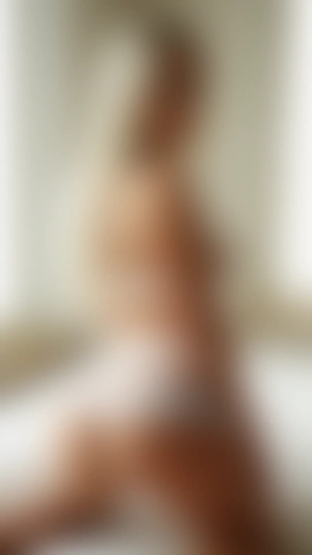 Blonde woman in sheer white lingerie kneeling on a white bed