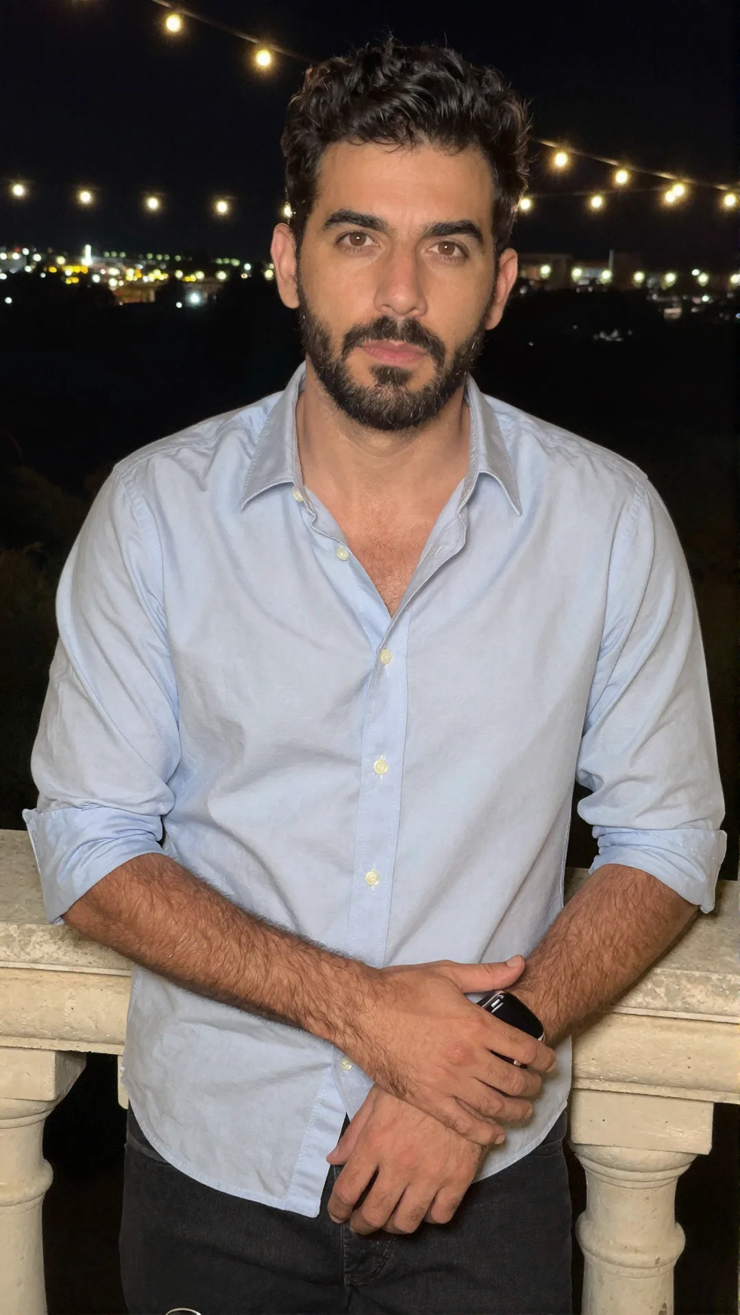 Serious Argentine man with rolled sleeves leaning on a terrace balustrade at night