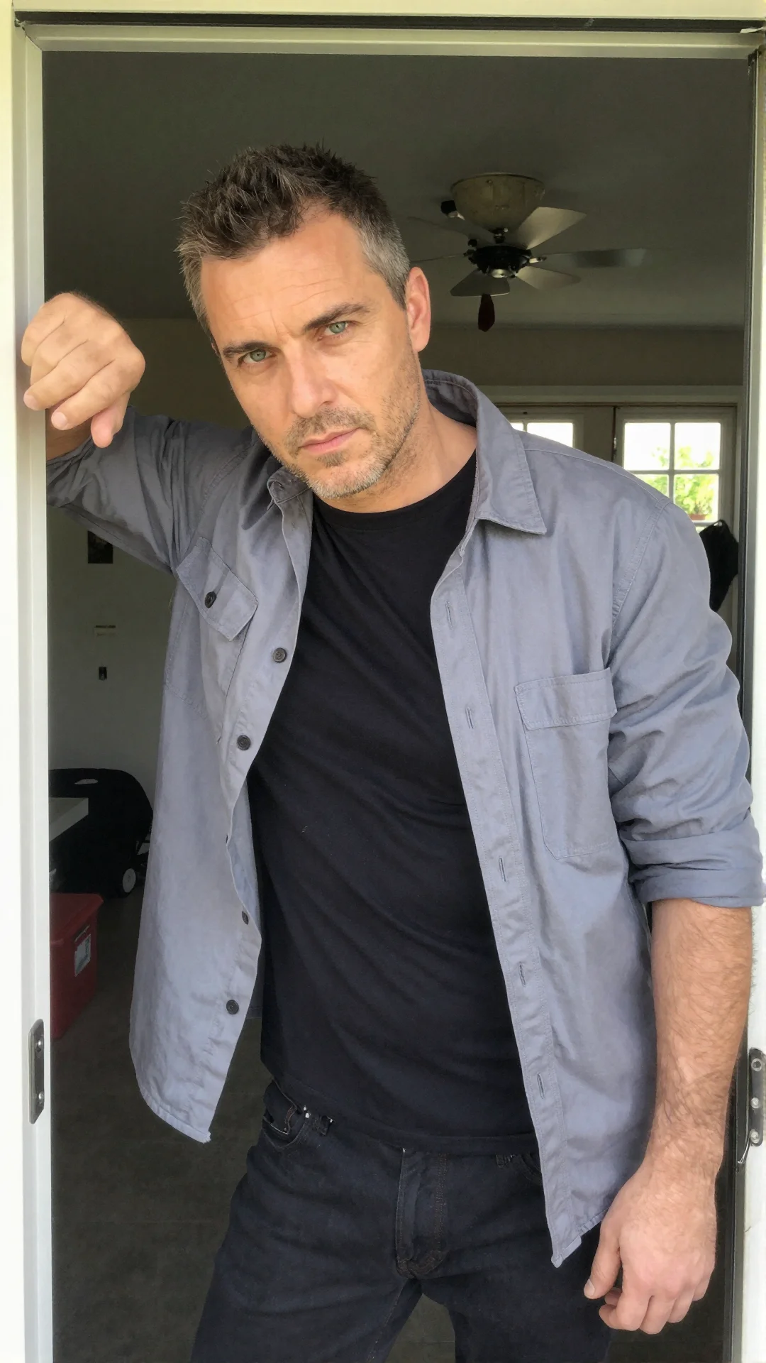 Serious Polish man in a rolled-sleeve work shirt leaning in a garage doorway