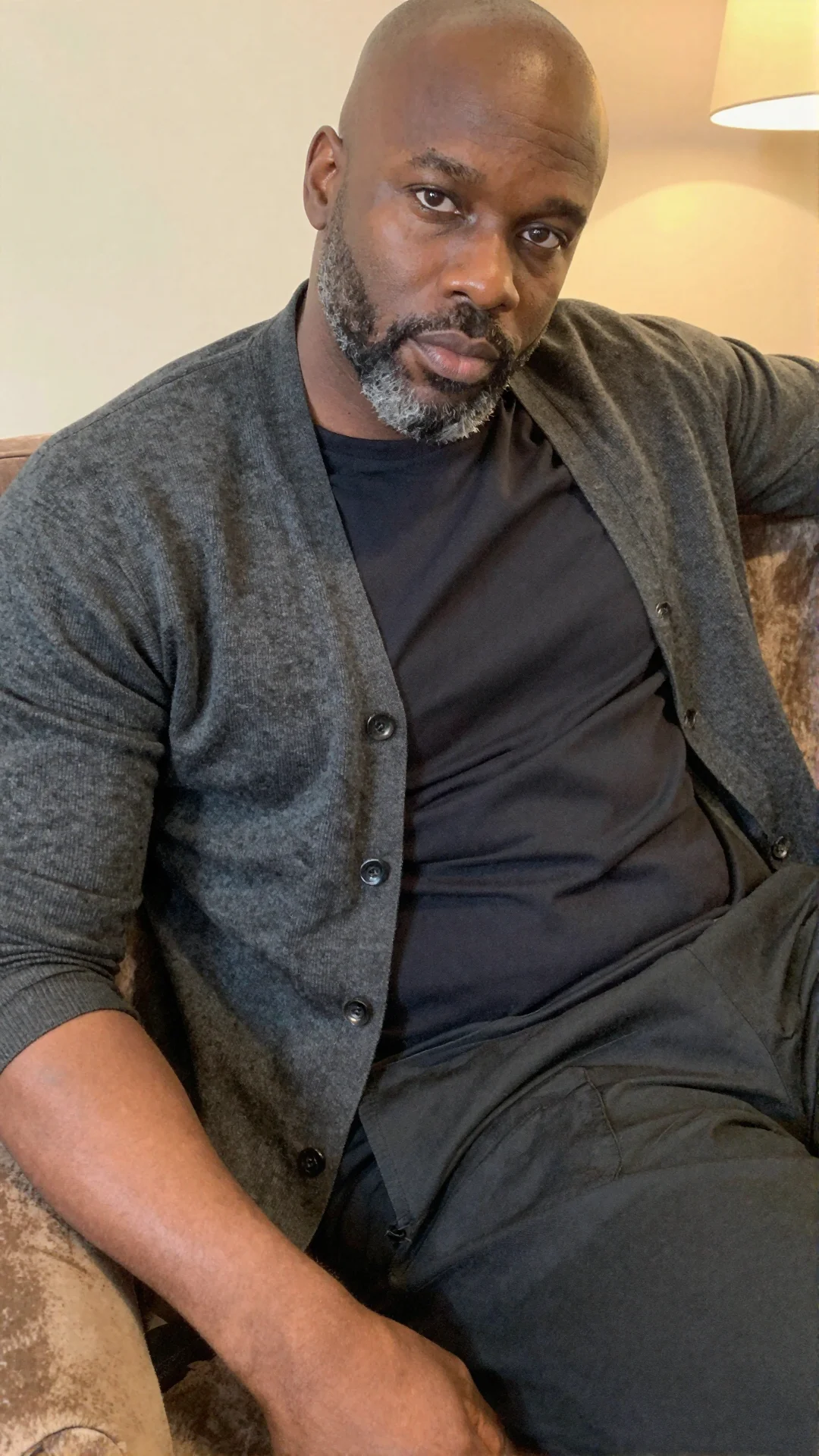 Serious Black British man in an unbuttoned cardigan on a velvet couch