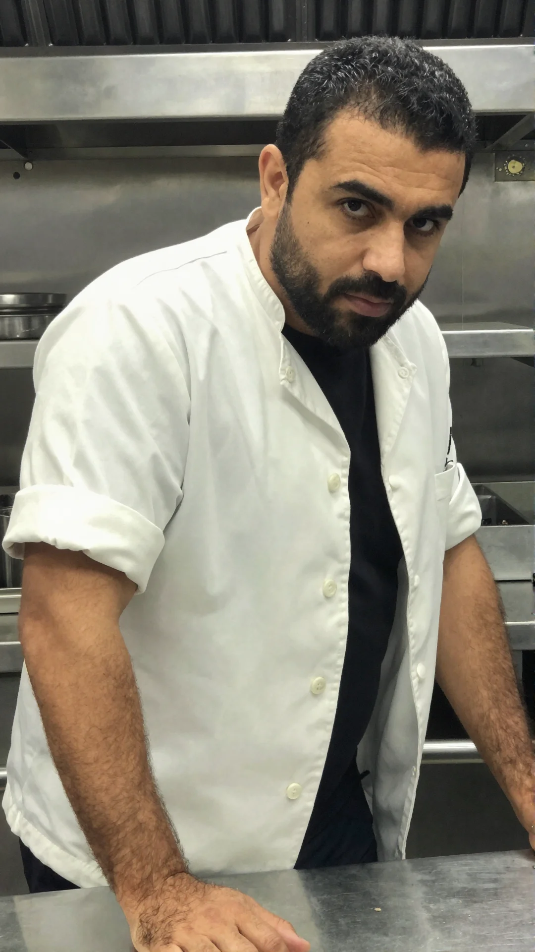 Serious Moroccan man in a chef's jacket leaning on a steel counter after service